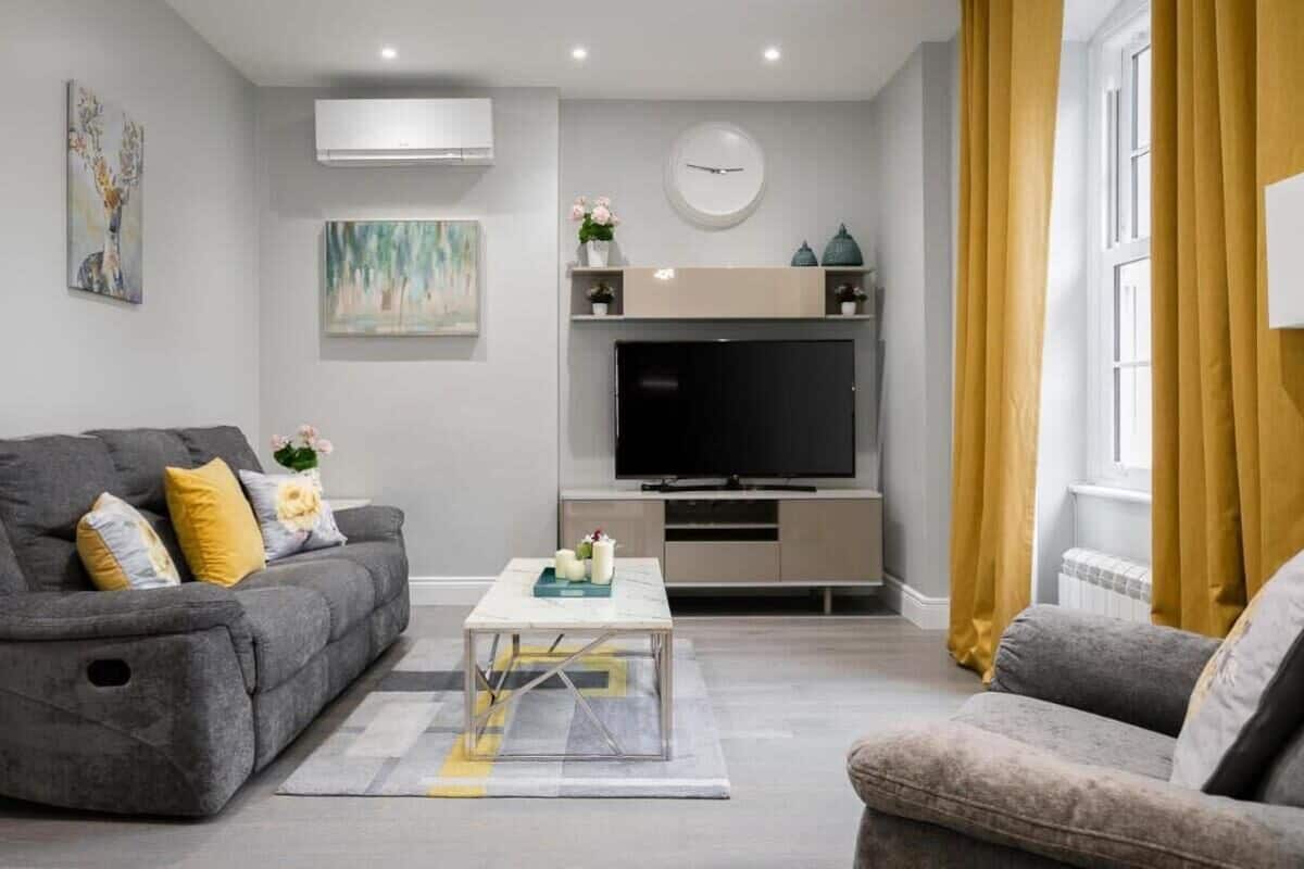 A modern living room with a grey sofa, a coffee table, a flat-screen TV, and a window with yellow curtains.