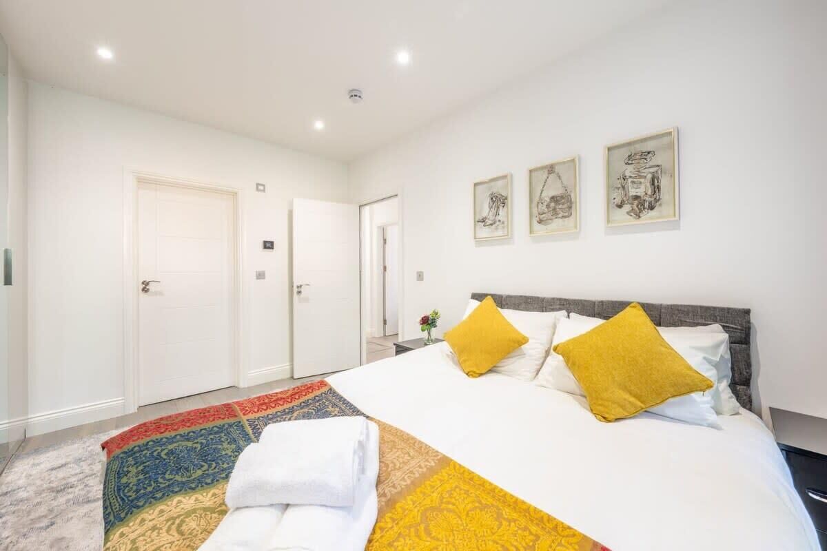 Habitación de hotel con una cama grande, dos almohadas amarillas, un tapete estampado y tres cuadros en la pared.