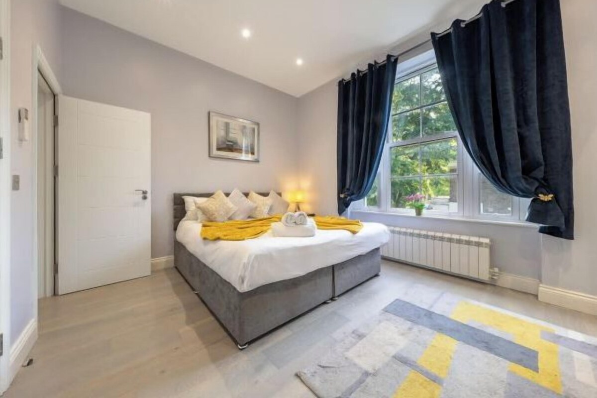 Un dormitorio con cama, lámpara de noche, ventana con cortinas y radiador.