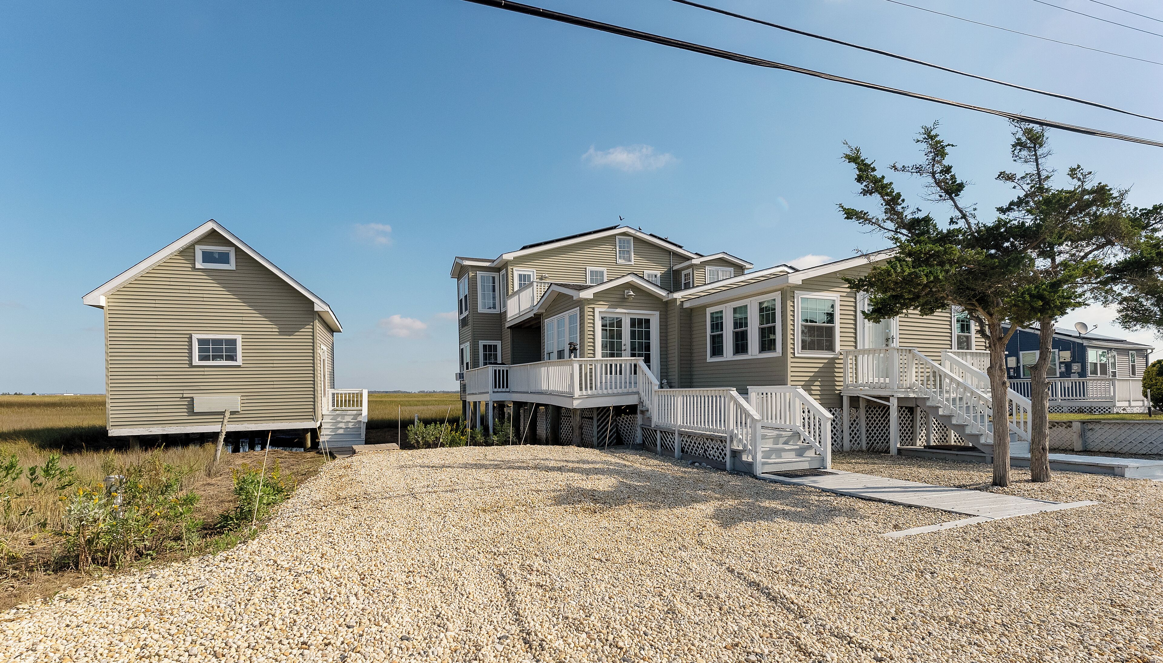 A coastal house with a gravel driveway, multiple decks, and a view of the ocean.