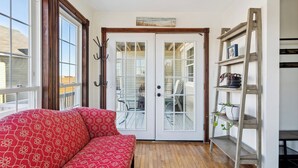 Ein Zimmer mit einem roten, gemusterten Sofa, einem Holzleiterregal mit Pflanzen und einer weißen Tür mit Glasscheiben.