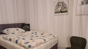 Un dormitorio con cama, una silla y un muro con cuadros.