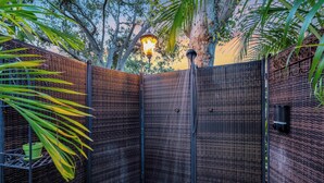 A corner garden with a metal fence, a wall-mounted light, and a small planter with a green pot.