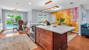 A modern kitchen with a large island, wooden cabinets, and a view of the backyard.