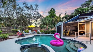 A backyard with a swimming pool, a pink flamingo float, and a hot tub.