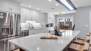 A modern kitchen with stainless steel appliances, a large island with a knife block, and a dining area with bar stools.