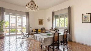 A dining room with a table set for four, a chandelier, and a view through large windows.