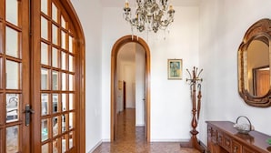 A hallway with a wooden door, a chandelier, a mirror, and a wooden cabinet.