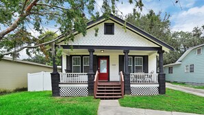A two-story house with a front porch, a red door, and a white picket fence. - Coastal Cottage near Winery (St. Augustine)