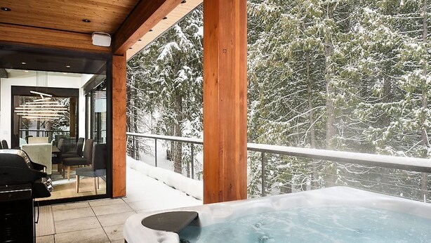 Un jacuzzi en un balcón con vistas a árboles nevados.