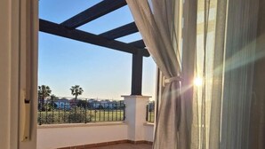 A balcony with a view of palm trees and a fence, a tiled floor, and a pergola structure.