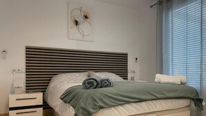 A modern bedroom with a bed, bedside tables, and a window with blinds.