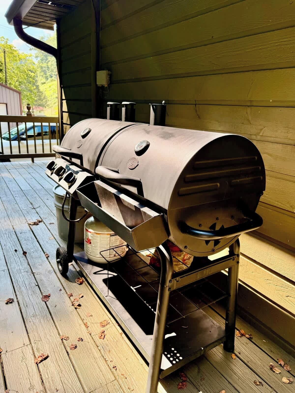 Un barbecue doté d’une cheminée, un chariot en métal et un récipient placés sur une terrasse en bois.