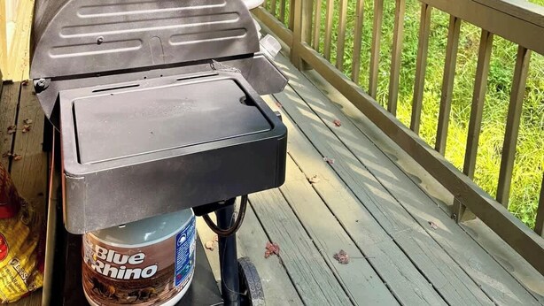 Una parrilla para barbacoa en una terraza de madera con vistas a una colina cubierta de césped y árboles.