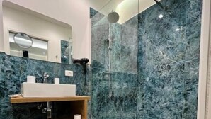 Un baño moderno con tocador de madera, cabina de ducha con vidrio y paredes de mármol.