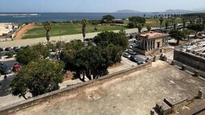 Una terraza en la azotea con vistas al mar, un estacionamiento y un edificio con columnas.