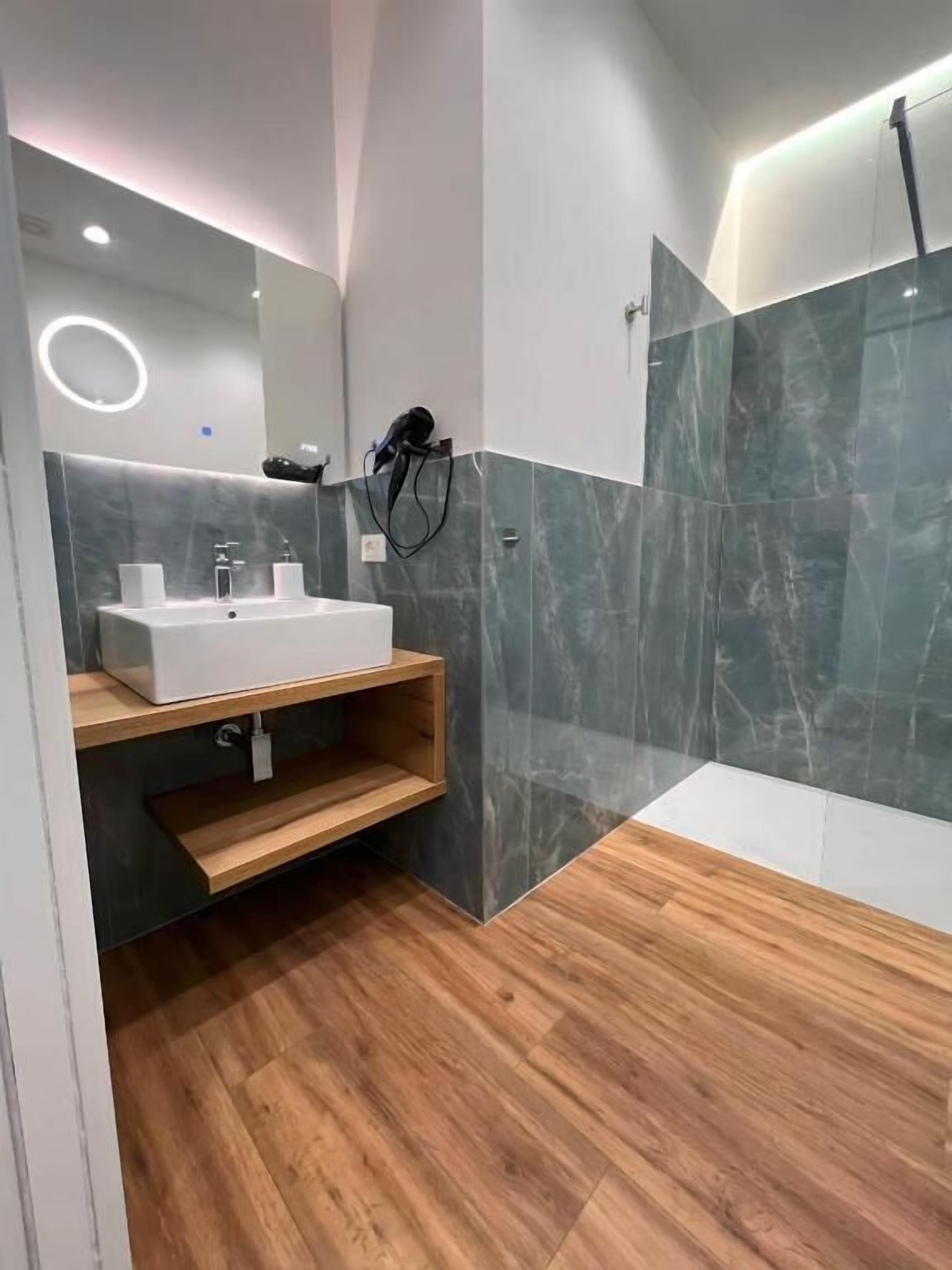 A modern bathroom with a wooden vanity, a white sink, and a large mirror.
