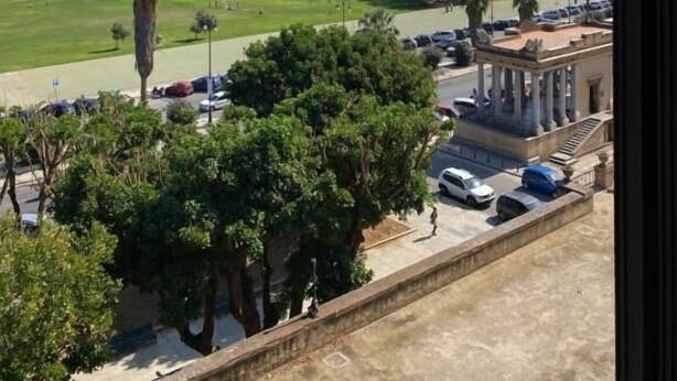 Vista de una zona costera con un estacionamiento, un edificio con columnas y un cielo azul despejado.