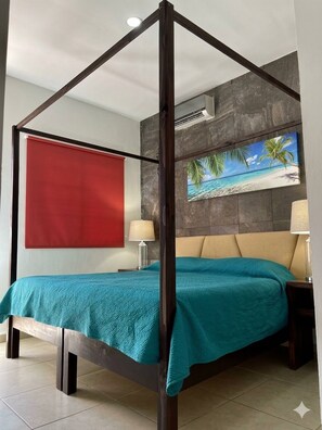 Een hemelbed met een turquoise deken, een rode wanddecoratie en een schilderij met een strandthema erboven.