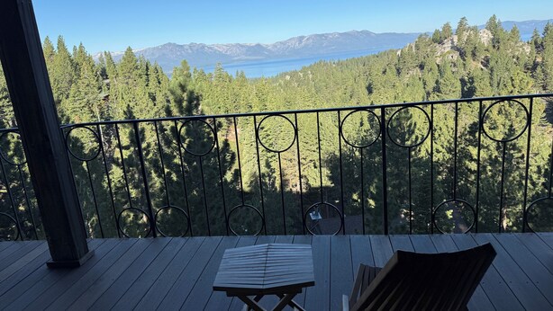 Un balcón con mesa y sillas de madera, con vistas a un bosque y montañas.