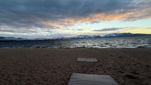 Una playa con un paseo marítimo de madera que conduce al agua, montañas al fondo y un cielo nublado.