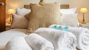 Ein ordentlich bezogenes Bett mit vielen Kissen und einem aufgerollten Handtuch.