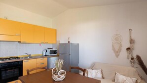 A compact kitchen with yellow cabinets, a gray refrigerator, a microwave, and a dining table with chairs.