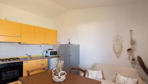 A compact kitchen with yellow cabinets, a gray refrigerator, a microwave, and a dining table with chairs. - Studio Boho by Propertize  - sea view Olbia (Olbia)