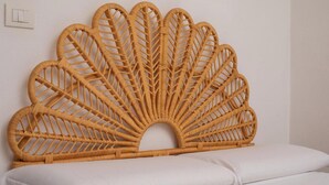 A room with a large woven headboard, a white bed, and a simple wall switch.
