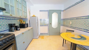 A compact kitchen with a stove, microwave, and coffee maker. There's a dining table with chairs and a patterned tile backsplash. - Havre de Paix Apt en Plein Centre de la Marsa (La Marsa)