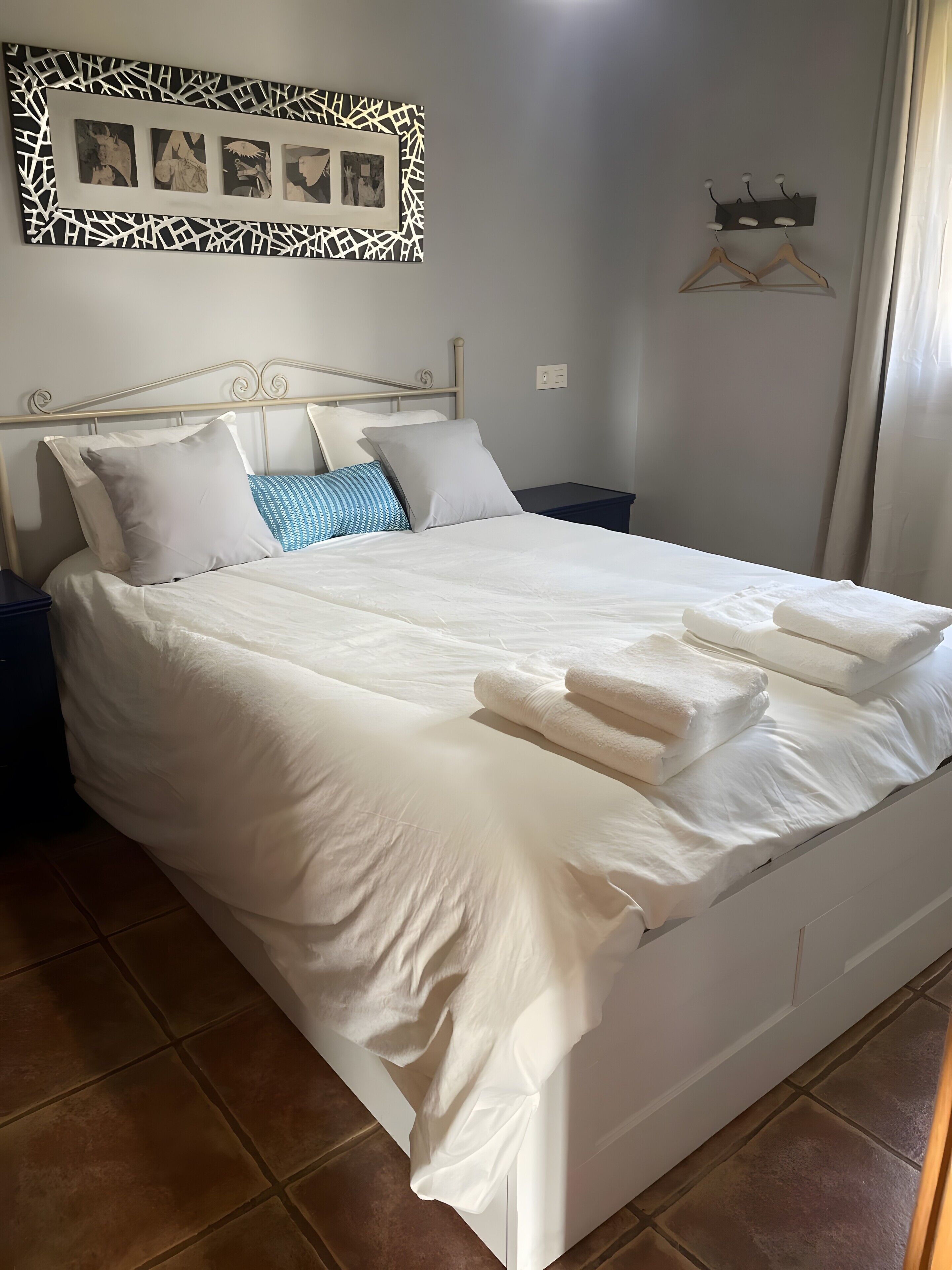 Een net opgemaakt bed met witte lakens, een hoofdbord en een aan de muur bevestigd fotolijstje.