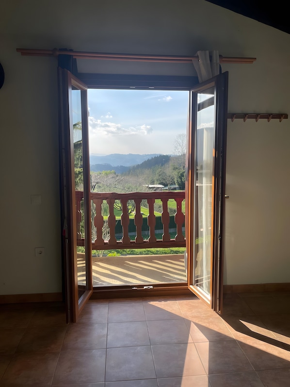 An open sliding door leading to a balcony with a view of a hilly landscape.