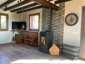 A living room with a fireplace, a television, a bench, and a clock on the wall.