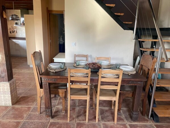 A dining area with a wooden table and chairs, a staircase, and a kitchen in the background.