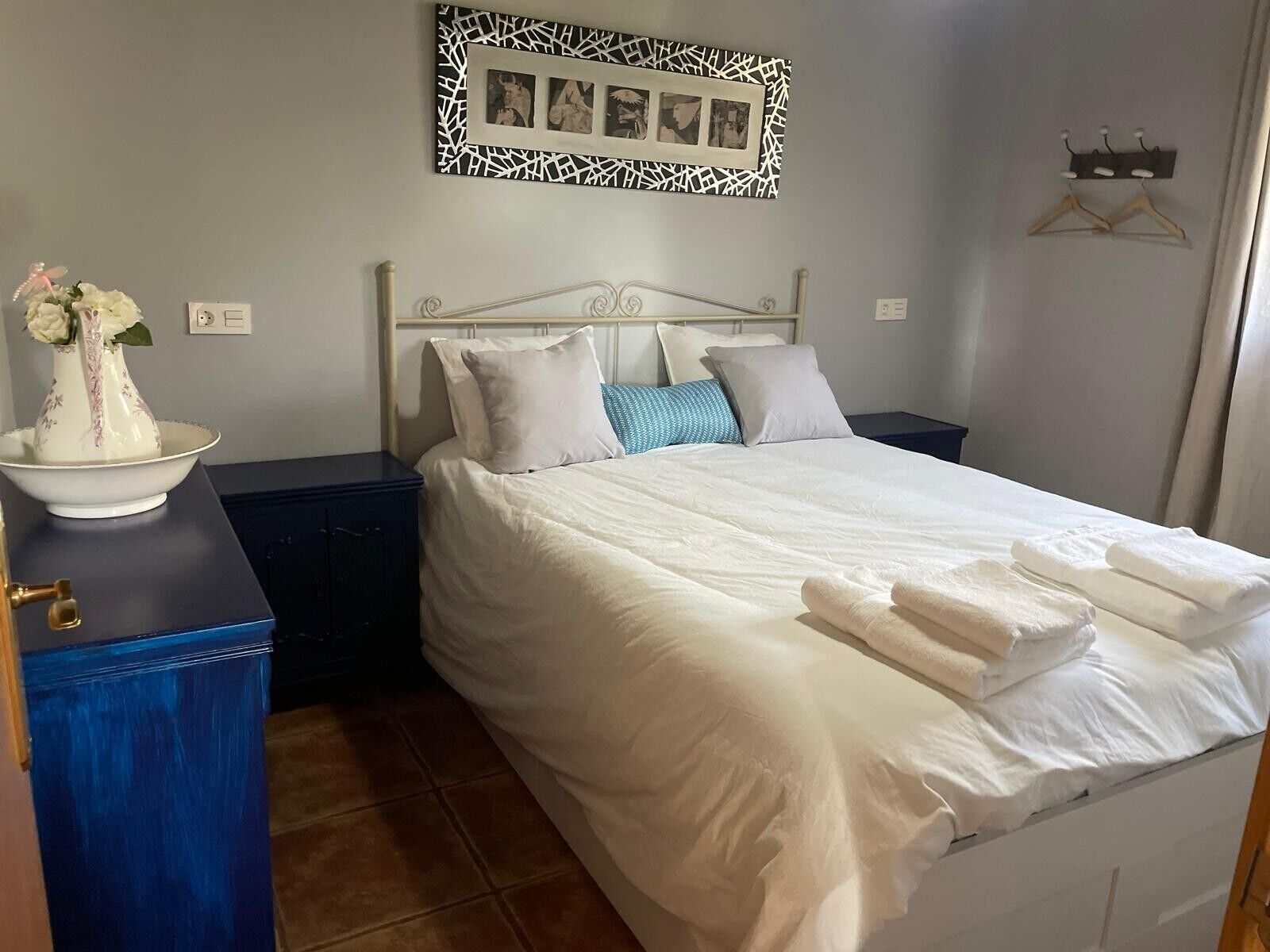 Una cama bien hecha con almohadas y un florero sobre una cómoda.