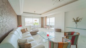 A spacious living room with a white sofa, a glass coffee table, and colorful armchairs.