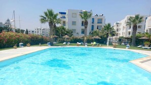 Una piscina rodeada de palmeras y sillas de descanso, con un edificio al fondo.