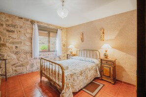 Ein Schlafzimmer mit einer Steinwand, einem Bett mit floralem Überwurf, zwei Nachttischlampen und einem Holznachttisch.