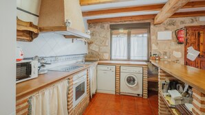 A kitchen with a microwave, oven, washing machine, and wooden beams.