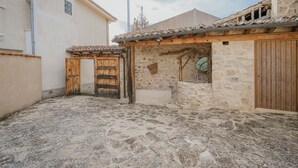 A courtyard with stone flooring, a wooden door, and a stone building with a tiled roof.
