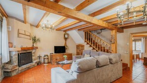 A living room with a fireplace, sofa, television, and wooden beams.