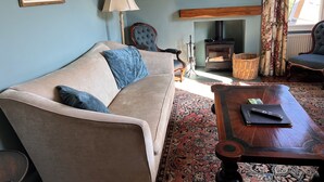 A living room with a beige sofa, blue cushions, a wooden coffee table, a fireplace, and two framed landscape paintings.
