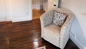 A room with a wooden floor, a patterned armchair, a rug, and a bathroom with a sink and mirror.