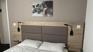 Un letto con testiera, un comodino, un telecomando e una lampada a parete.