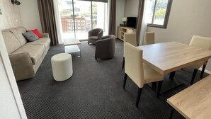 Una moderna camera d'hotel con divano, poggiapiedi, tavolo da pranzo, sedie, televisione e una grande finestra con vista.