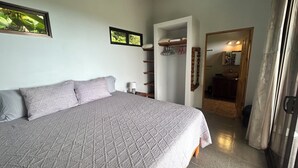 Un dormitorio con una cama grande, una mesita de noche, un armario y un baño visible a través de una puerta abierta.