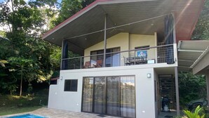 Una casa de dos pisos con piscina, balcón cubierto y garaje.