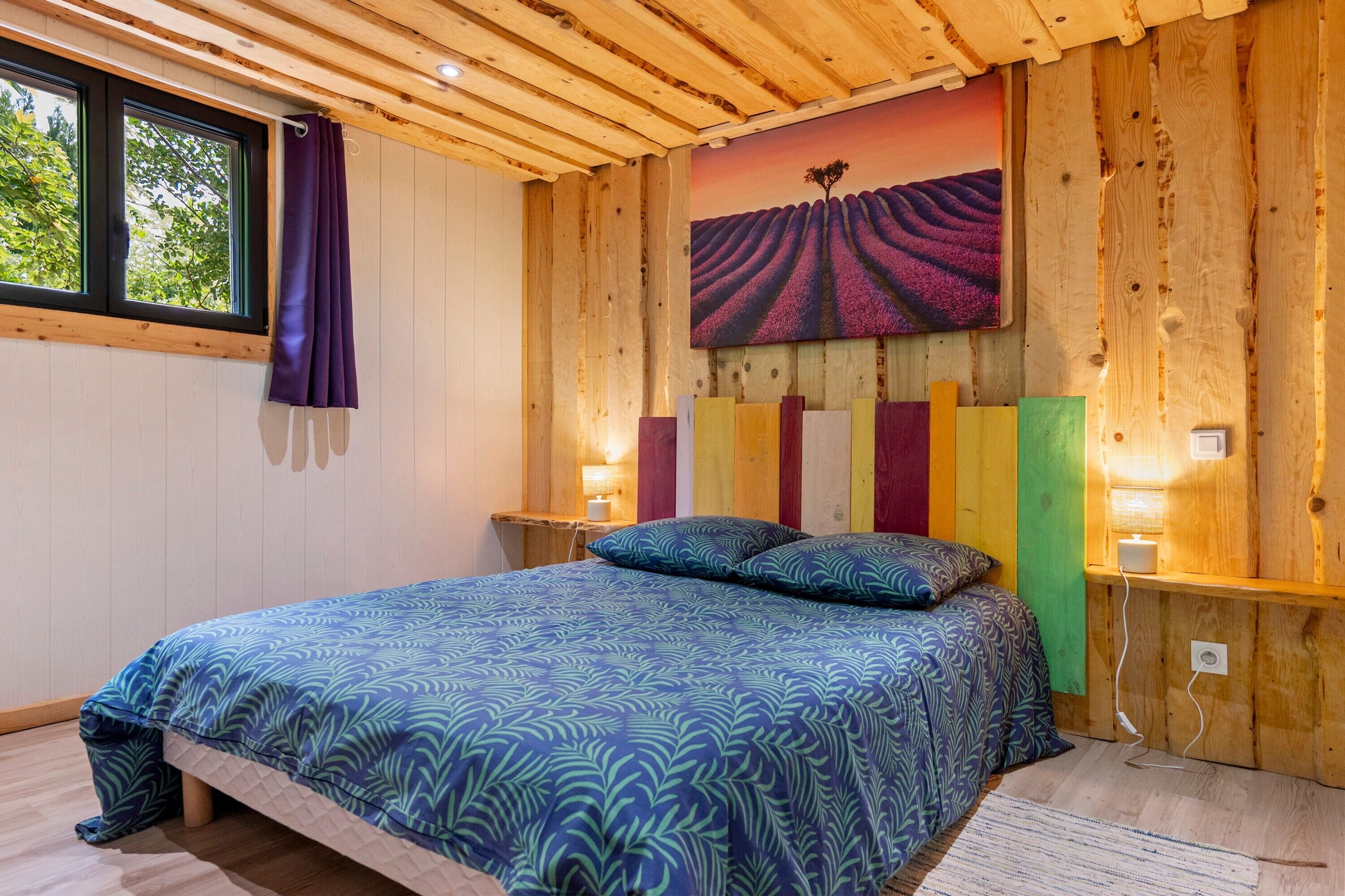 Una habitación con cama, ventana con cortinas, panel decorativo en la pared y un cuadro.