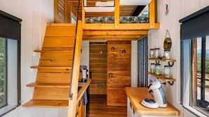 Interior de madera compacto con varios niveles, una escalera, una zona de cocina con cafetera y una ventana con vistas.