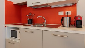 Una cocina compacta con un lavamanos de acero inoxidable, una cafetera y un microondas.